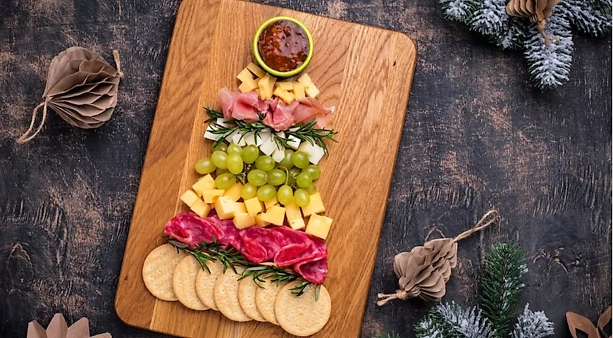 Demokratická verze prkénka Charcuterie z plátků masa, sýrů a hroznů ve tvaru vánočního stromku pro slavnostní tabuli.